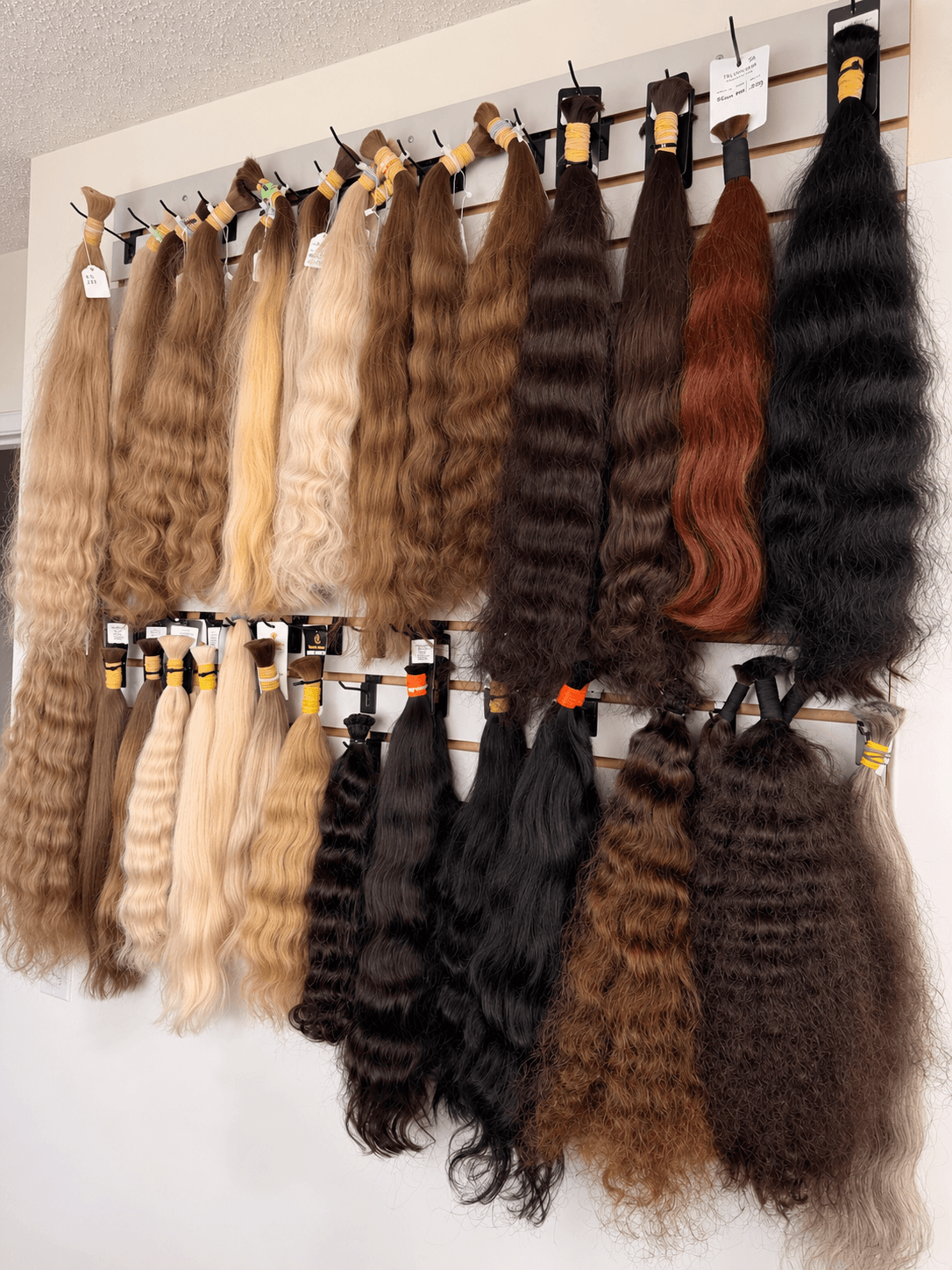 Hair bundles in blonde, brown and dark shades, with straight, wavy and curly textures, arranged on a studio rail.